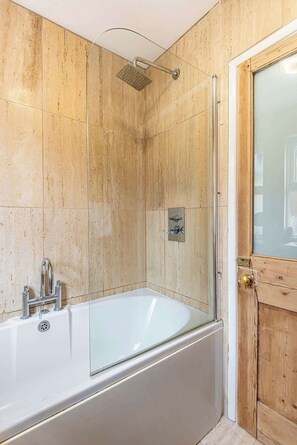 Ein Badezimmer mit einer Glaskabine zur Badewanne, einer Duschbrause und einer Holztür.