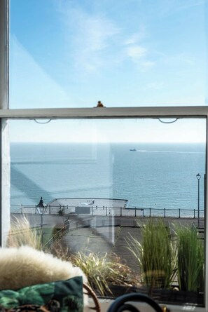 Blick auf das Meer von einem Fenster mit Blick auf eine Promenade, an der sich ein GelÀnder und ein Laternenpfahl befinden.