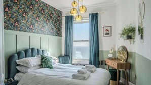A bedroom with a bed, a desk, a chair, a window with curtains, and a wall with a floral pattern. - The Wellington - style, charm, stunning sea views (Ramsgate)