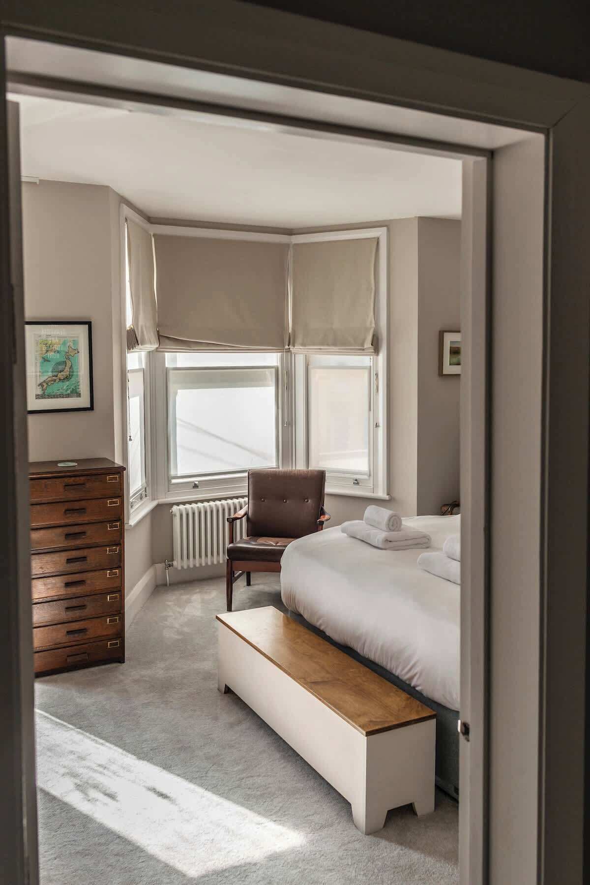 Une chambre à coucher comprenant un lit, un banc, une chaise, une commode et un radiateur.