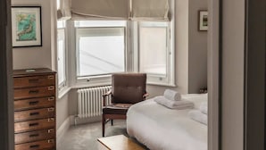 Une chambre à coucher comprenant un lit, un banc, une chaise, une commode et un radiateur.