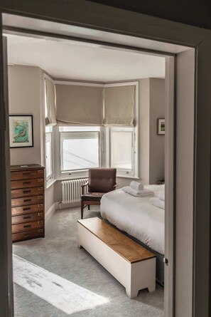 A bedroom with a bed, a bench, a chair, a dresser, and a radiator.
