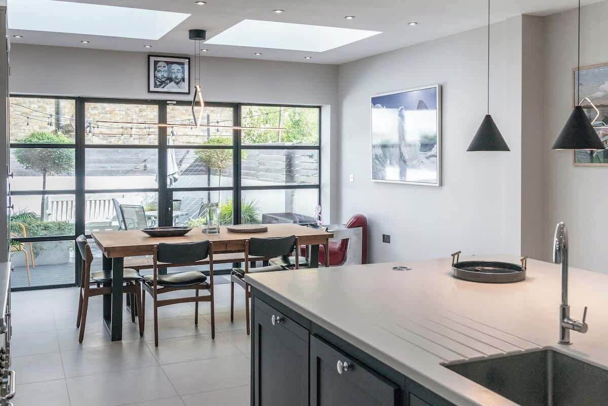 Une cuisine moderne dotée d’un grand îlot central, d’un coin repas avec des chaises, d’une grande fenêtre et d’œuvres d’art accrochées aux murs.