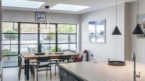 Une cuisine moderne dotée d’un grand îlot central, d’un coin repas avec des chaises, d’une grande fenêtre et d’œuvres d’art accrochées aux murs.