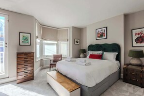 Una habitación de hotel con una cama grande, un banco, un aparador, una silla y una ventana.