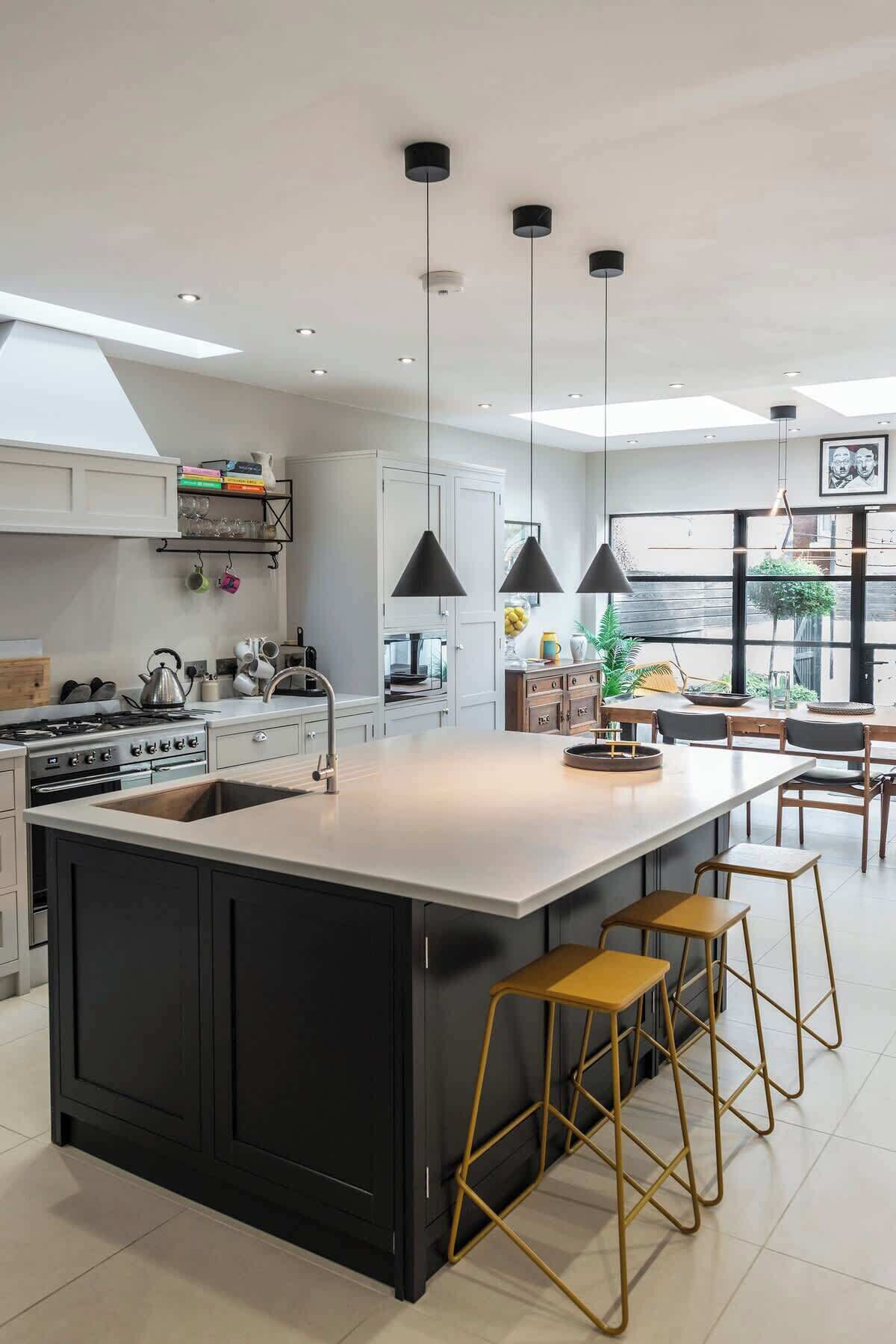 Une cuisine moderne dotée d’un îlot central, de luminaires suspendus et offrant une vue sur l’extérieur.