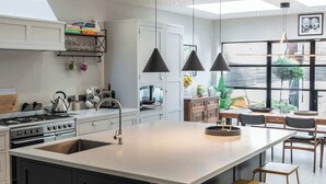 Une cuisine moderne dotée d’un îlot central, de luminaires suspendus et offrant une vue sur l’extérieur.