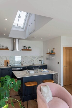 A modern kitchen with a skylight, marble countertops, and a central island with bar stools.