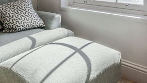 Une pièce avec une grande fenêtre, un canapé, un coussin à motifs et un lampadaire.