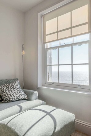 A room with a large window, a sofa, a patterned pillow, and a floor lamp.