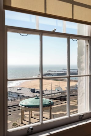 A view through a window of a beach with a promenade, a lighthouse, and a pier.