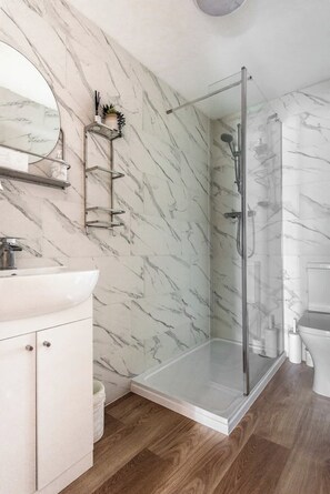 Un bagno moderno con una parete in marmo, una cabina doccia in vetro, un lavandino bianco e un water.