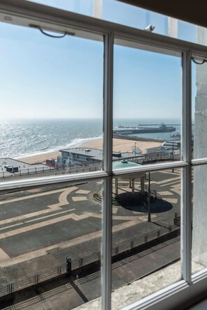 A view through a window of a coastal area with a beach, a pier, and a large ship docked at a port. - Wellington Retreat- modern, stylish, sea-views (Ramsgate)