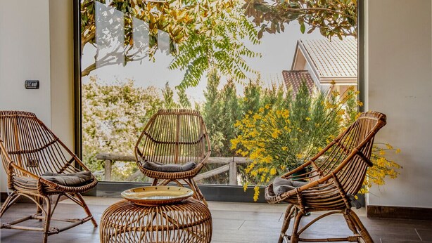 A room with two wicker chairs, a small table, and a view of trees and buildings through a large window. - Ville Petrara: villa con piscina e spa nei vigneti (Poppano San mango sul calore)