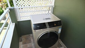 A compact, stainless steel Whirlpool washer and dryer unit in a small laundry room with a tiled floor and a white lattice partition. - Newly constructed luxury apartment. -Pristine Stay- (Roseau)