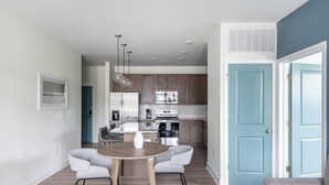 A modern kitchen with stainless steel appliances, a dining area with a round table and two chairs, and a light blue door.