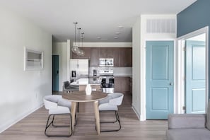 A modern kitchen with stainless steel appliances, a dining area with a round table and two chairs, and a light blue door.