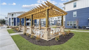 A covered outdoor seating area with brick pillars and chairs, surrounded by a landscaped garden with grass and shrubs.