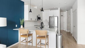 A modern kitchen with white cabinets, a stainless steel refrigerator, and a bar area with two wooden chairs.