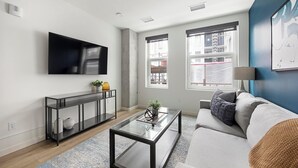 A modern living room with a flat-screen TV, a glass coffee table, a sofa, and a console table with decorative items.