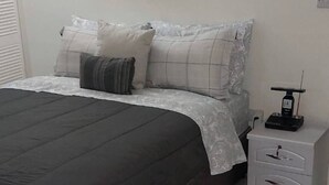 Un dormitorio con cama, mesita de noche, lámpara y un cuadro en la pared.