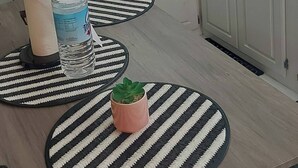 Cocina con armarios blancos, microondas, estufa a gas, tostadora y licuadora sobre la encimera. Hay una botella de agua y un rollo de toallas de papel sobre la mesa.