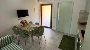 Ein Essbereich mit einem Tisch für zwei Personen, einem an der Wand montierten Fernseher und einer Tür zu einem anderen Raum.