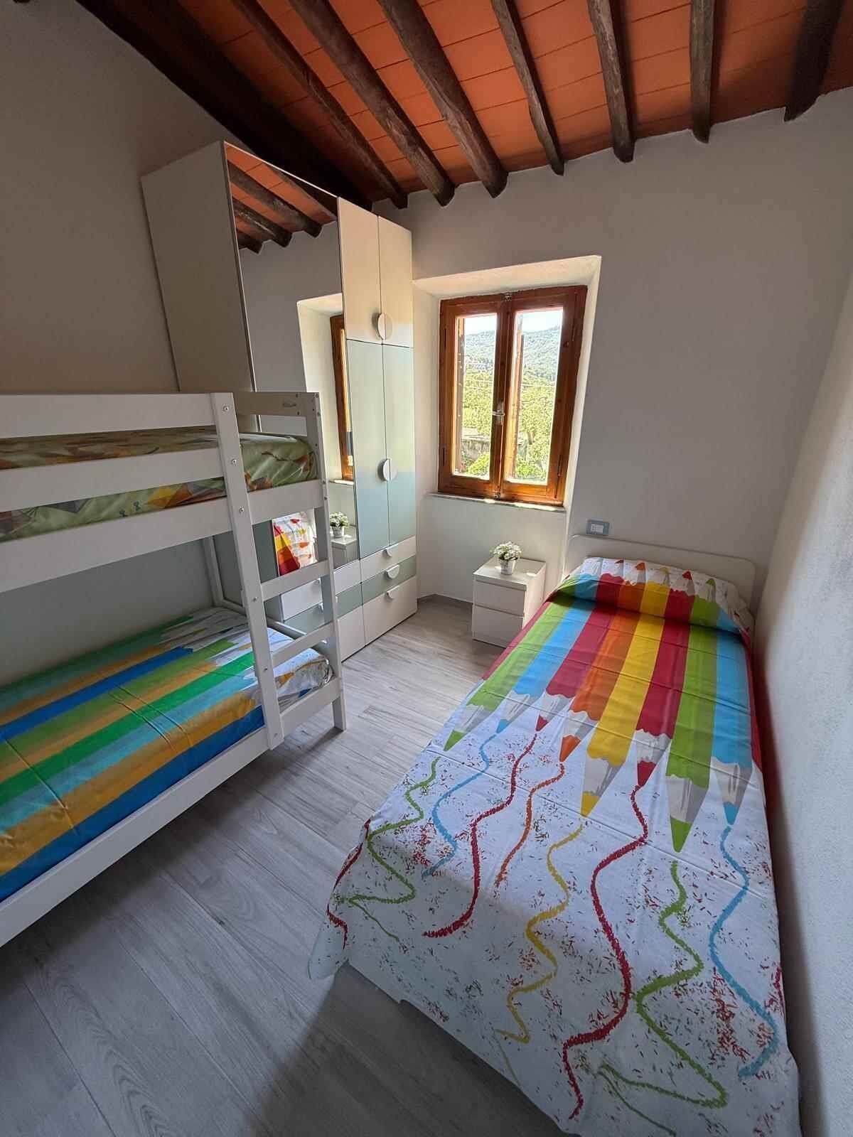A bedroom with bunk beds, a wardrobe, a small bedside table, and a window with a view.