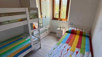 A bedroom with bunk beds, a wardrobe, a small bedside table, and a window with a view.