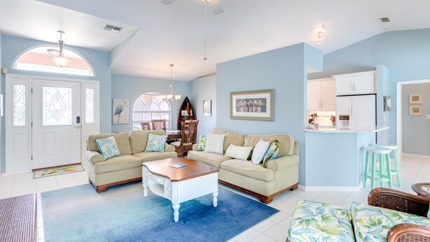 A spacious living room with a ceiling fan, a dining area with a chandelier, and a kitchen with white cabinets. - Family Friendly Home in Naples, Near Beach, Heated Pool, Dog Friendly (Naples)