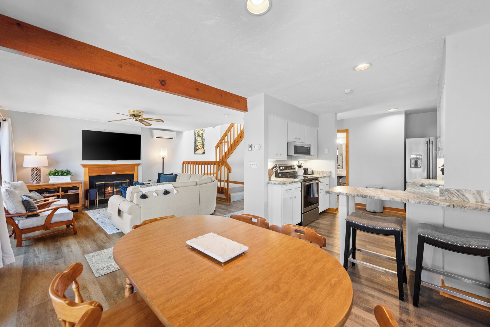 A modern living space with a wooden dining table, a fireplace, a TV, and a kitchen area.