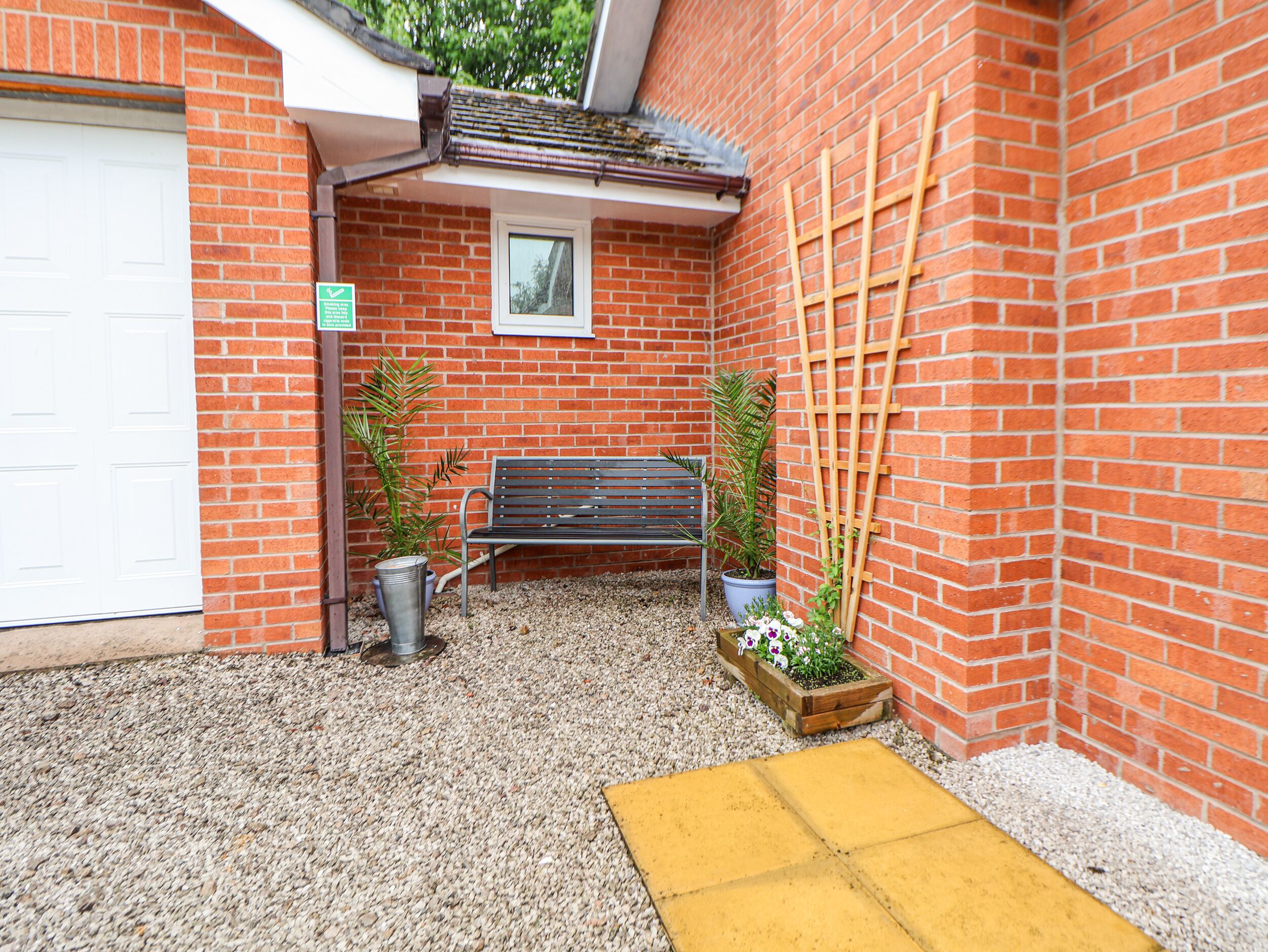 A small outdoor area with a bench, potted plants, and a yellow mat.