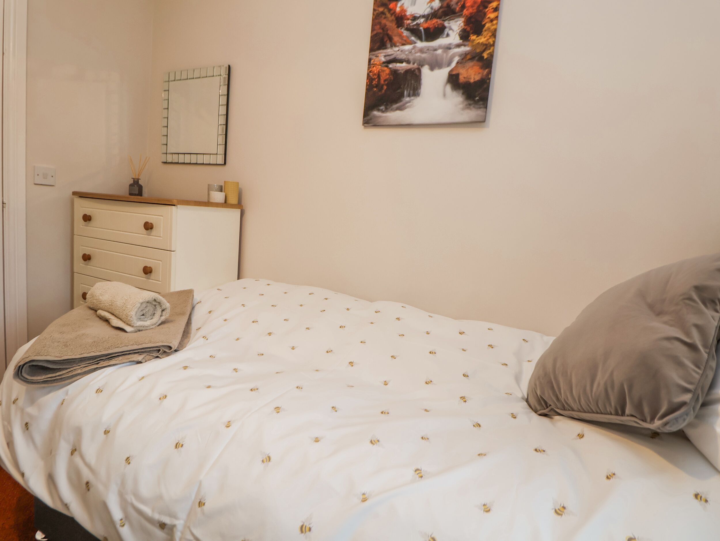 A bedroom with a bed, a dresser, a mirror, and a painting on the wall.