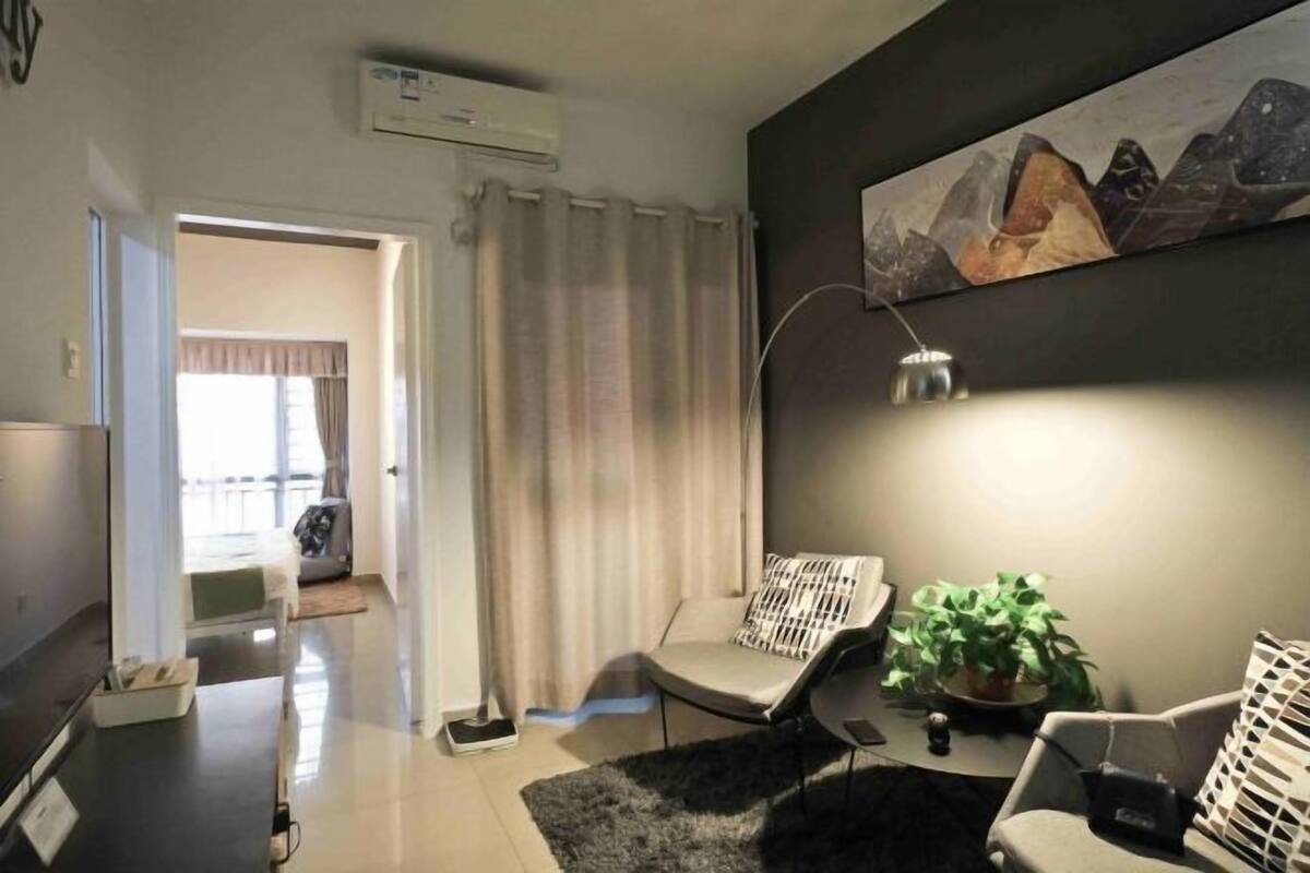 Un salon moderne avec un téléviseur à écran plat, un canapé, un fauteuil, une lampe et un tableau accroché au mur.