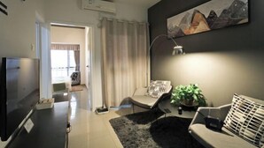Ein modernes Wohnzimmer mit Flachbildfernseher, einer Couch, einem Sessel und einem Bild an der Wand.