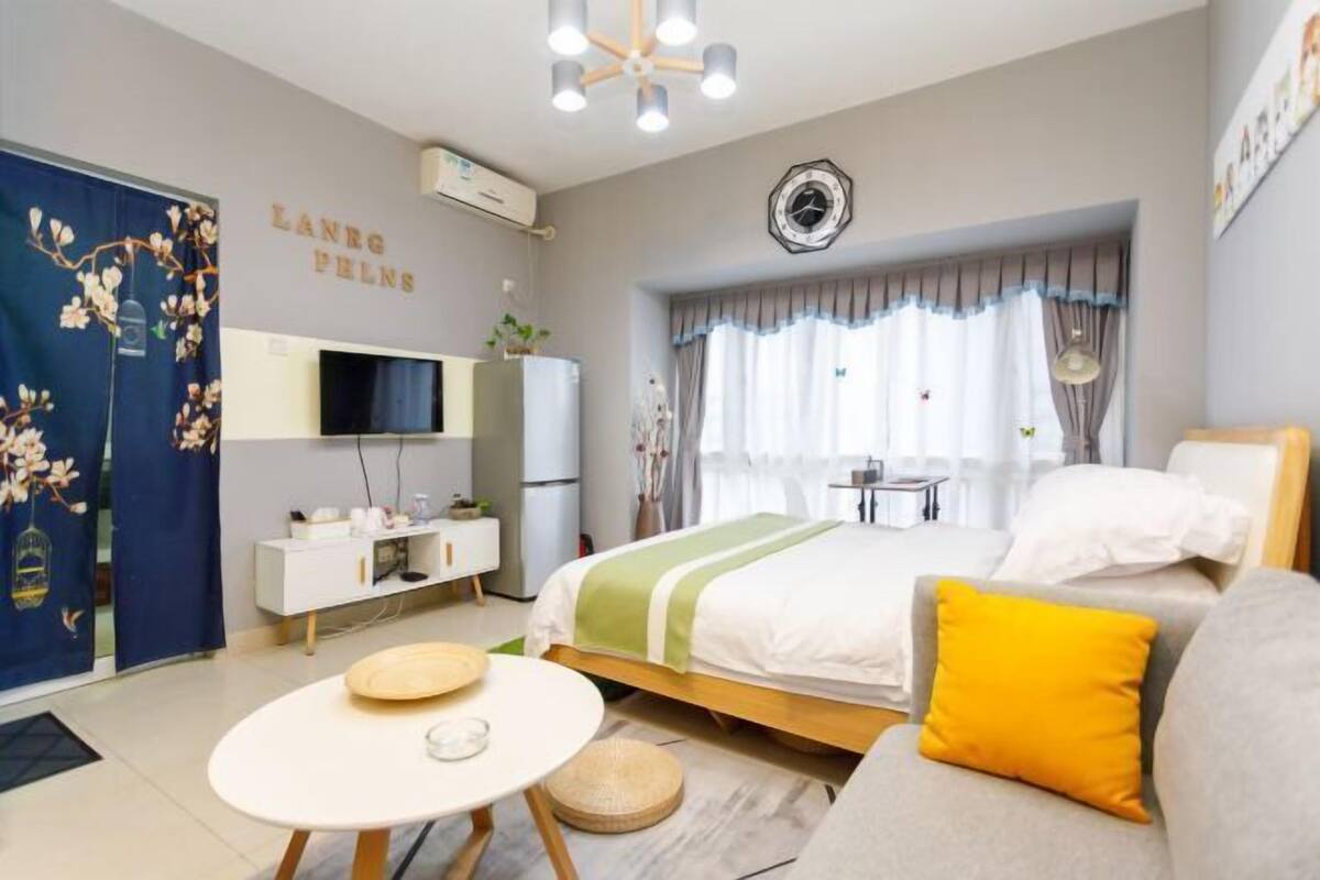Une chambre d’hôtel avec un lit, un canapé, une télévision, un bureau et une fenêtre avec des rideaux.