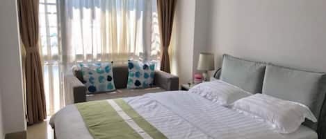 A hotel room with a bed, a sofa, a nightstand, and a window with curtains.