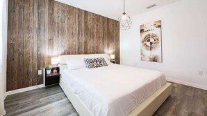 A bedroom with a wooden accent wall, a bed with white bedding, a geometric pendant light, and a framed picture on the wall. - 9 Ensuite Resort Villa with Private Pool/SPA/BBQ (Kissimmee)