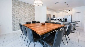 A modern dining area with a wooden table and black chairs, a stone accent wall, and a kitchen in the background. - 9 Ensuite Resort Villa with Private Pool/SPA/BBQ (Kissimmee)