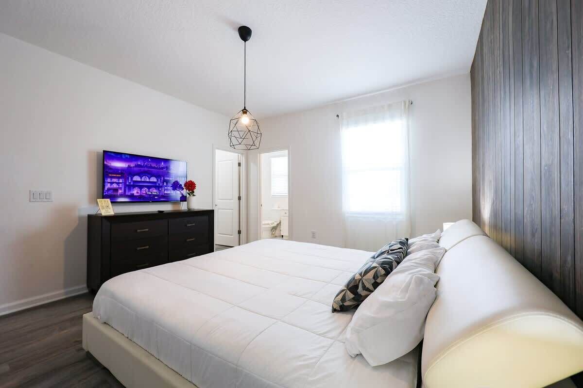 Une chambre à coucher comprenant un lit, un téléviseur, une commode et un luminaire suspendu.