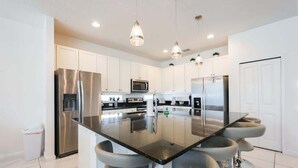 A modern kitchen with stainless steel appliances, a central island with bar stools, and pendant lighting. - 9 Ensuite Resort Villa with Private Pool/SPA/BBQ (Kissimmee)