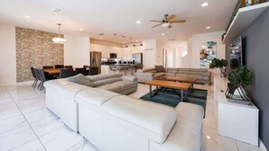 A modern living room with a sectional sofa, a dining area, a kitchen, and a staircase leading to an upper level. - 9 Ensuite Resort Villa with Private Pool/SPA/BBQ (Kissimmee)