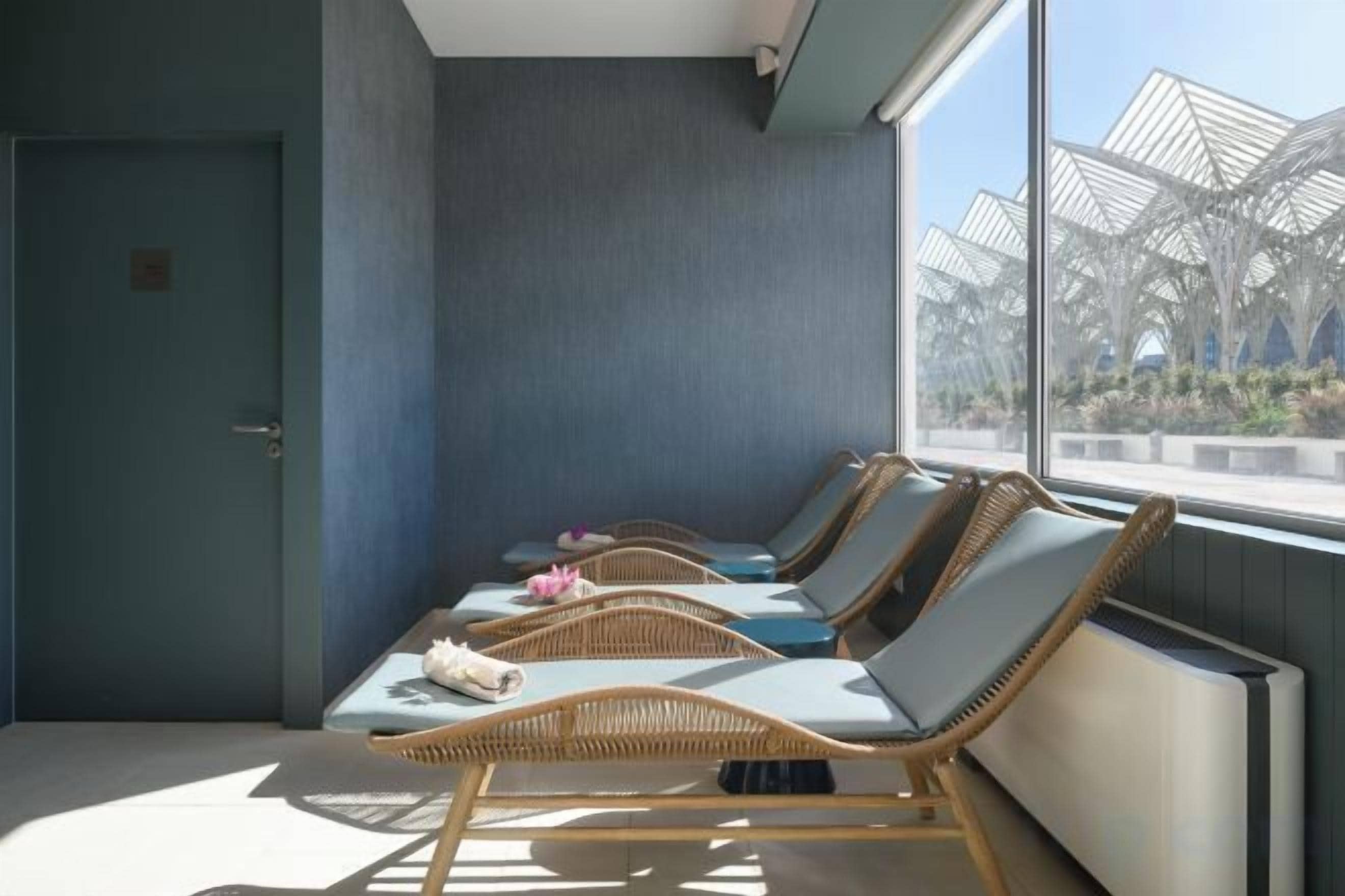 Una habitación con cuatro sillones de mimbre, una puerta y un ventanal con vistas a una estructura exterior.