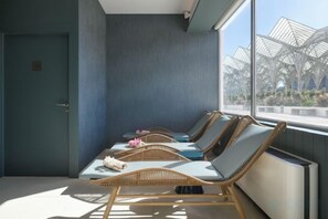 Ein Zimmer mit vier Korbsesseln, einer Tür und einem großen Fenster mit Blick auf eine Außenarchitektur.