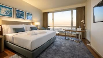 A hotel room with a large bed, a desk, a chair, and a view of the beach.