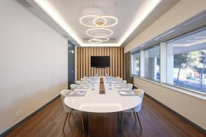 Une salle de conférence équipée d’une longue table, de chaises, d’un téléviseur à écran plat et d’une fenêtre donnant sur un paysage agréable.