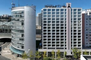 Un hotel moderno con fachada curva, un llamativo letrero 'HOTEL MEILA' y vistas claras del entorno urbano.