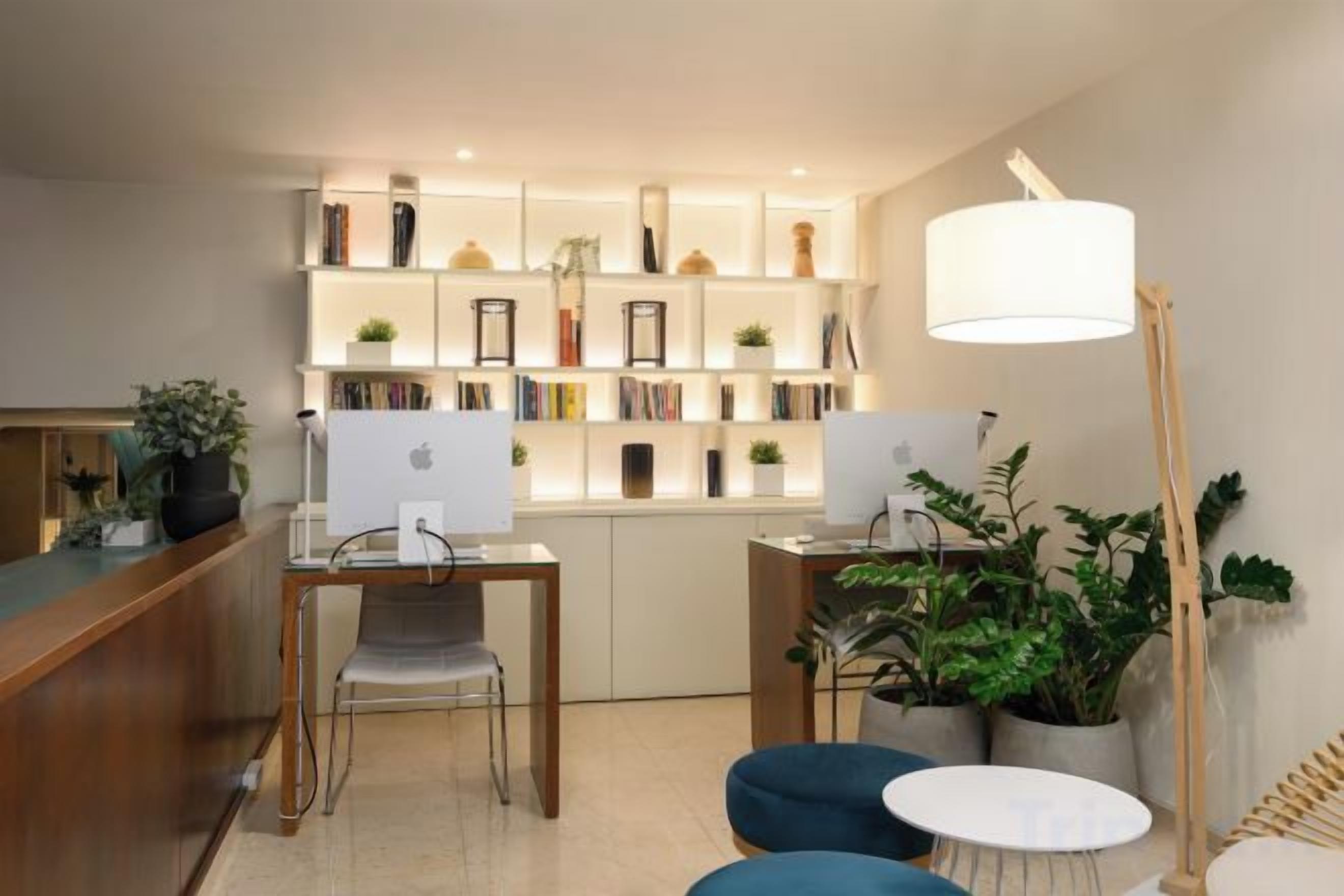 Un espace de bureau moderne comprenant deux bureaux, des chaises, une bibliothèque et une lampe.