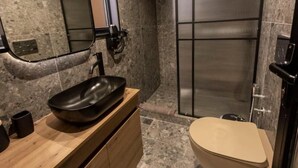 Ein modernes Badezimmer mit einer Naturstein-Arbeitsplatte, einem schwarzen Waschbecken, einer beige gefärbten Toilette und einer Duschkabine aus Glas.