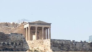 Une structure classique avec des colonnes, peut-être un temple ou un ancien édifice, avec un mur de pierre au premier plan.